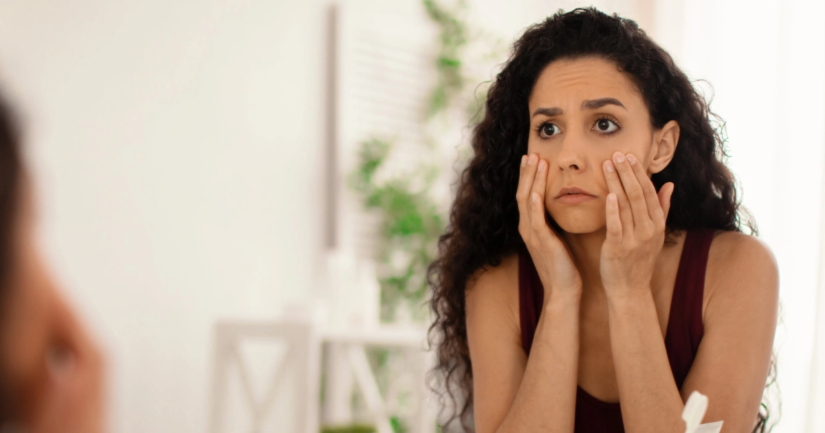 Woman checking under-eye concerns in the mirror, considering Eye Treatments at Brandish Clinic Facial and Skin Rejuvenation in La Jolla, CA